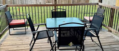 A wooden deck with a table and chairs, a covered area, and a view of the backyard.