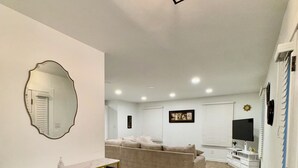 A modern living room with a sofa, a TV, a mirror, and a staircase.
