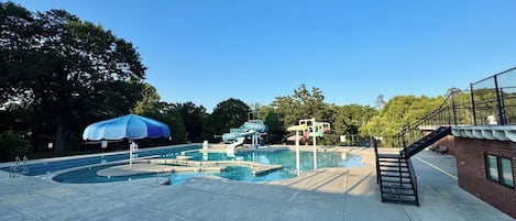 A swimming pool area with a slide, a covered seating area, and a staircase leading to a building.
