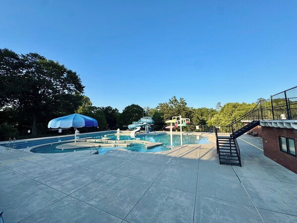 A swimming pool area with a slide, a covered seating area, and a staircase leading to a building.