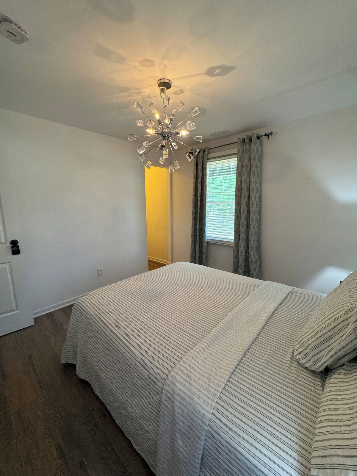 A bedroom with a bed, a ceiling light fixture, a window with curtains, and a door.