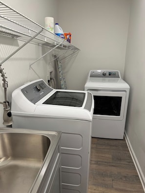 A laundry area with a front-loading washer and dryer, a metal shelf with laundry supplies, and a stainless steel sink.