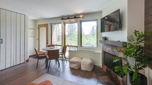 Ett modernt kök med en öppen spis, stora fönster och en matplats med stolar och ett bord.