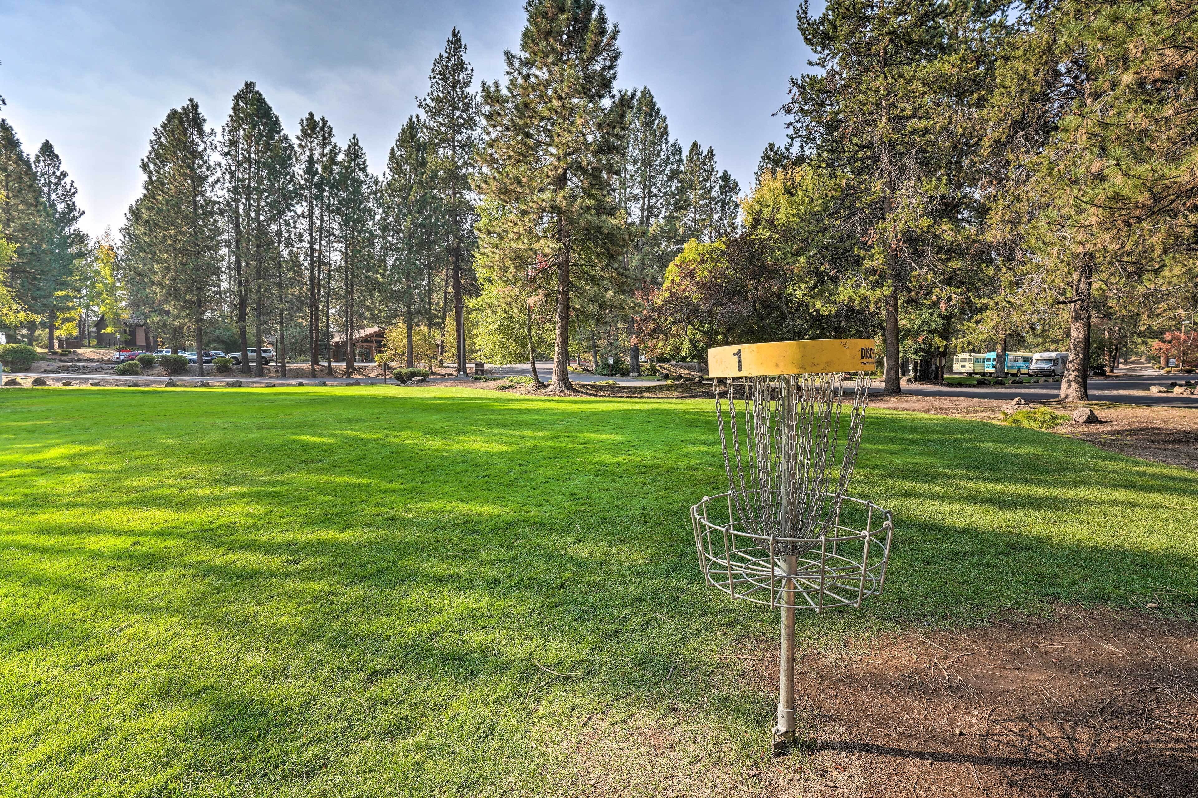A park with a disc golf basket, a yellow sign, and a blue and white train in the background.