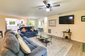 Ein Wohnzimmer mit Sofa, Couchtisch, Fernseher und einer Küche im Hintergrund.