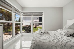 Ein Schlafzimmer mit großem Fenster, einem Bett mit gemustertem Überwurf und zwei aufgerollten Handtüchern auf dem Bett.