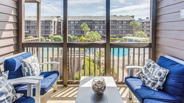 Un balcon offrant une vue sur un ensemble d’immeubles, une piscine et un espace salon extérieur.