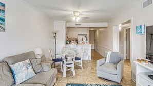 Un salon comprenant un canapé, des fauteuils, une table basse et un meuble pour la télévision. Il y a également un coin cuisine avec une table à manger et des chaises.