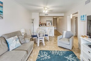 Een woonkamer met een bank, fauteuils, een salontafel en een tv-meubel. Er is ook een keukenhoek met een eettafel en stoelen.