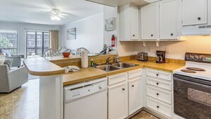 Une cuisine avec des meubles blancs, un lave-vaisselle, une cuisinière et une machine à café.