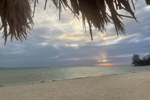 Ein Strand mit freiem Blick auf den Ozean und einem Sonnenuntergang in der Ferne.