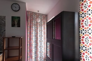 Ein Zimmer mit einem gemusterten Vorhang, einer Wanduhr und einem dunklen Schrank.