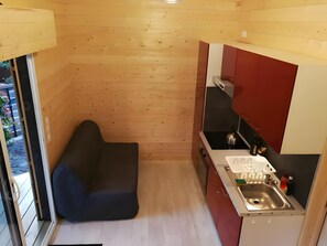 A compact kitchen with wooden walls, a built-in stove, a sink, and a small seating area. - Holiday Home “La Cabane – Bassin d’Arcachon” with Shared Pool and Private Garden (Gujan-Mestras)