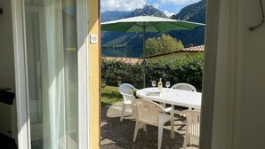 Ein Zimmer mit einer Schiebetür zu einer Terrasse im Freien, inklusive Tisch, Stühlen und einem grünen Sonnenschirm.