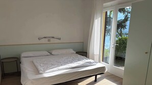 Ein Schlafzimmer mit einem Bett, einem Nachttisch, einem Fenster mit Vorhängen und Blick ins Grüne.
