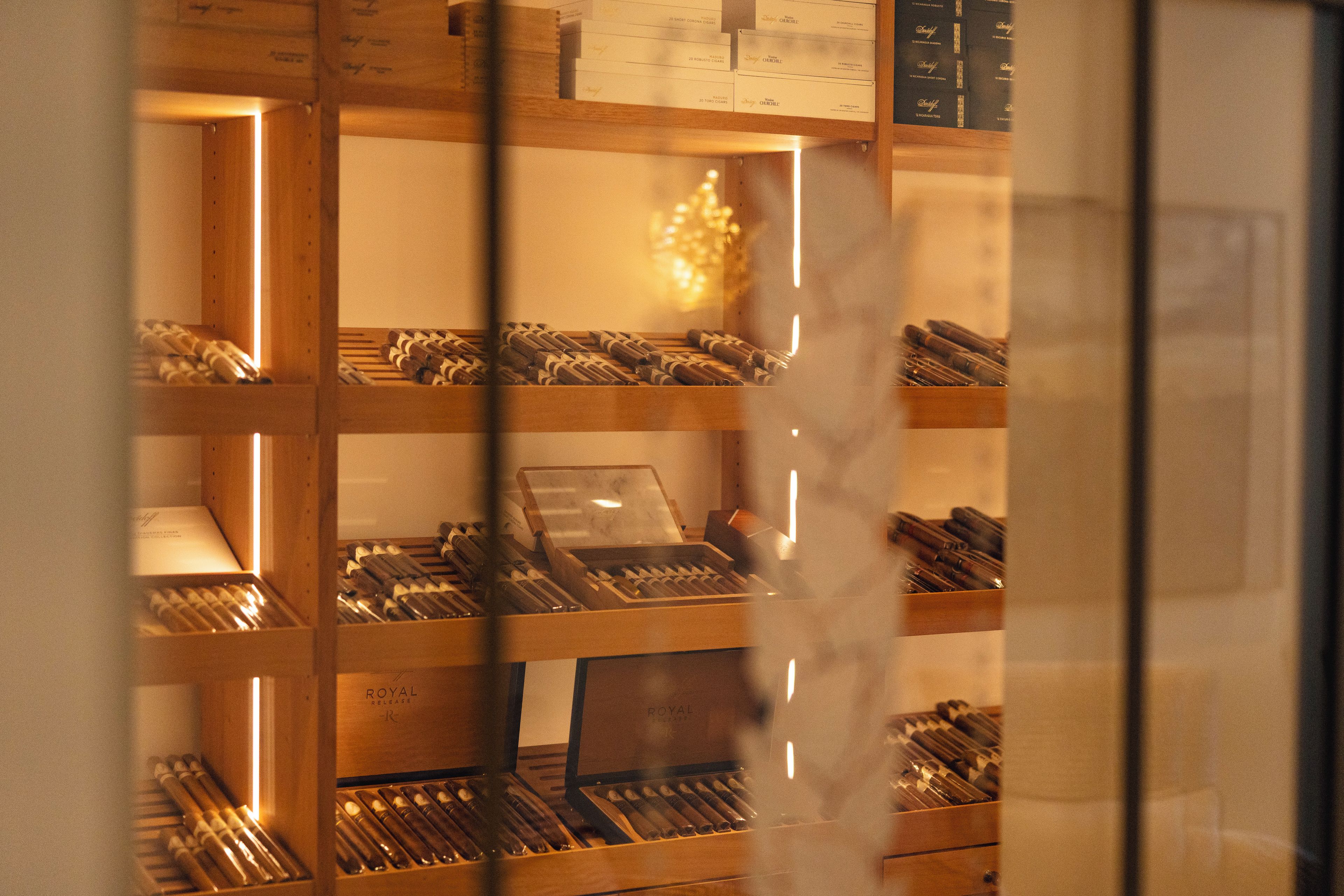 Exhibición de cigarros en cajas de madera, con un menú arriba y una partición de vidrio al frente.