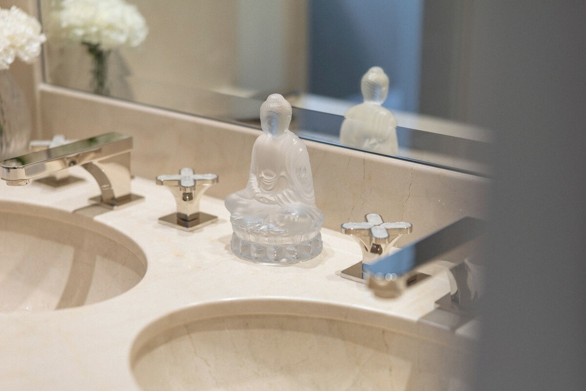 A bathroom with a large mirror, a sink, and a decorative glass Buddha statue.