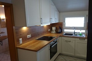 Eine kleine Küche mit weißen Schränken, einer Holz Arbeitsplatte, einem Einbauofen und einem Fenster über dem Spülbecken.