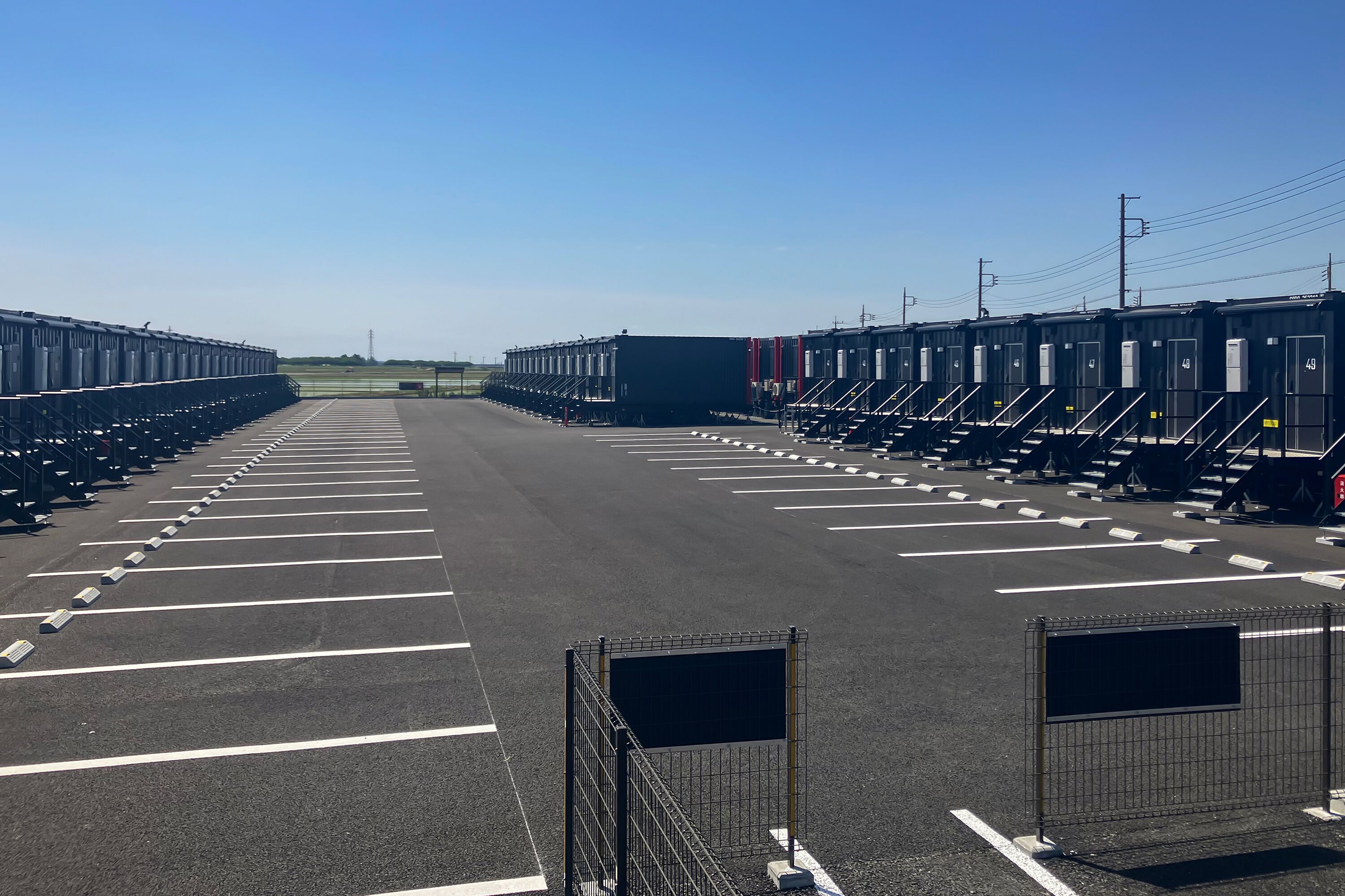 A parking lot with rows of black containers, white parking lines, and a clear sky.