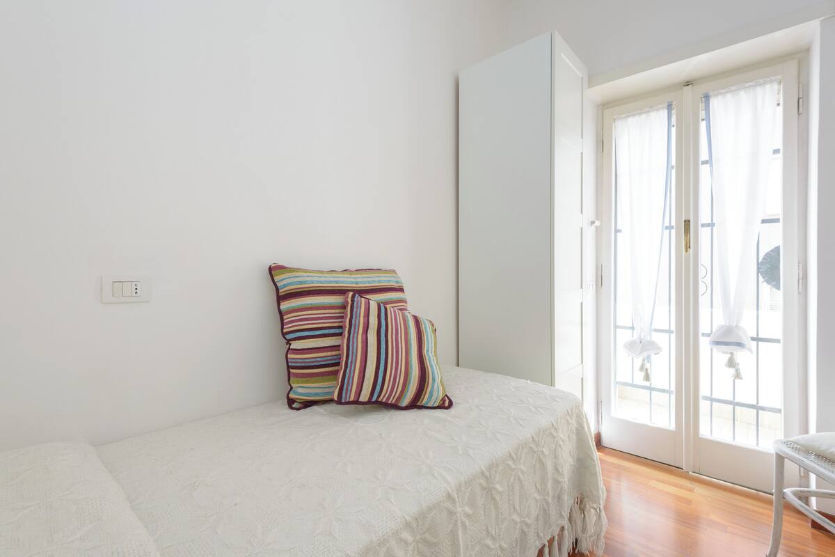 Een slaapkamer met een bed, een raam met gordijnen en een deur.