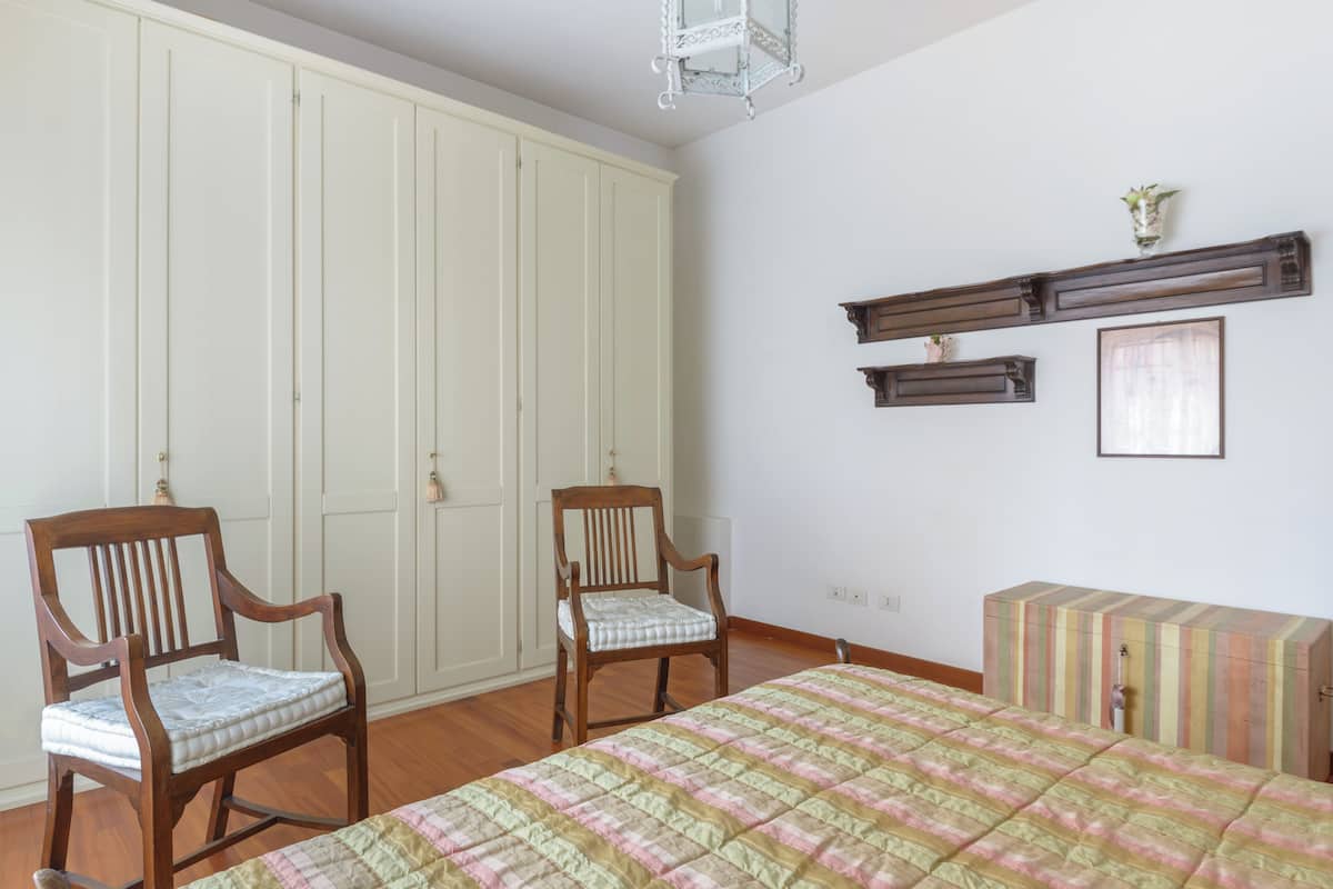 Een slaapkamer met een bed, twee stoelen, een kledingkast en een dressoir.