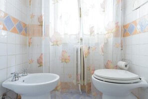 Et badeværelse med vask, toilet og bruseforhæng med blomstermønster.