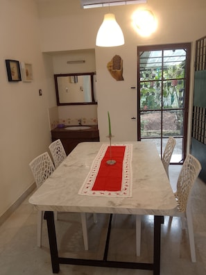 A dining table with a red runner, surrounded by white chairs, in a room with a window and a door leading outside.