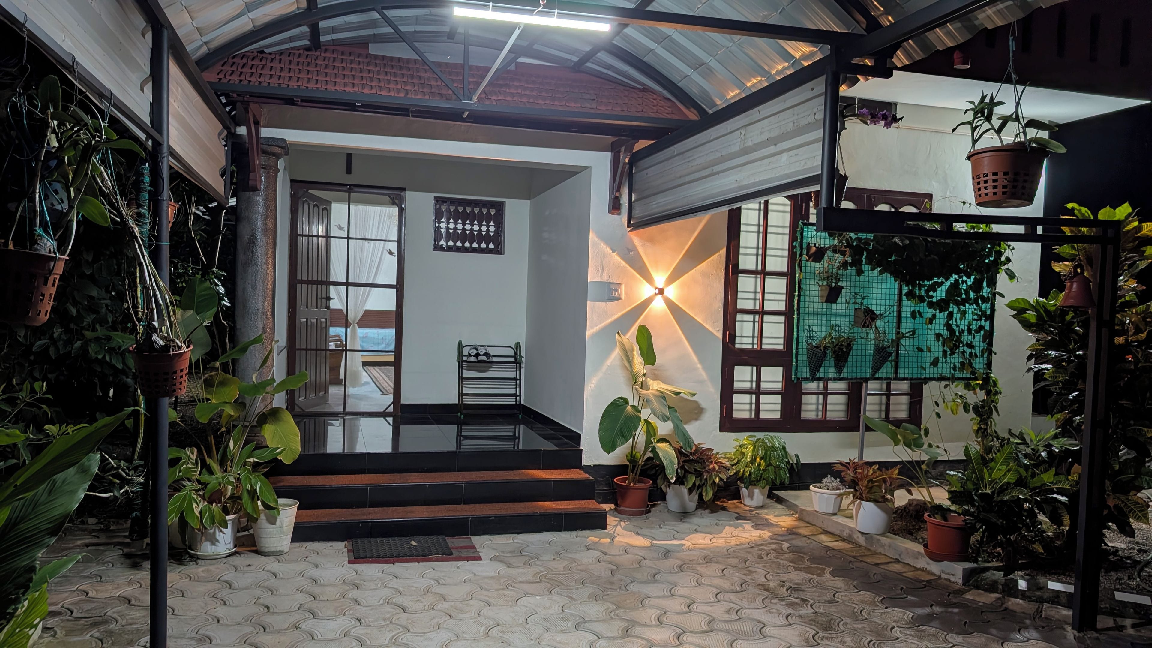 A covered outdoor area with steps leading to a balcony, surrounded by potted plants and a wall-mounted light fixture.