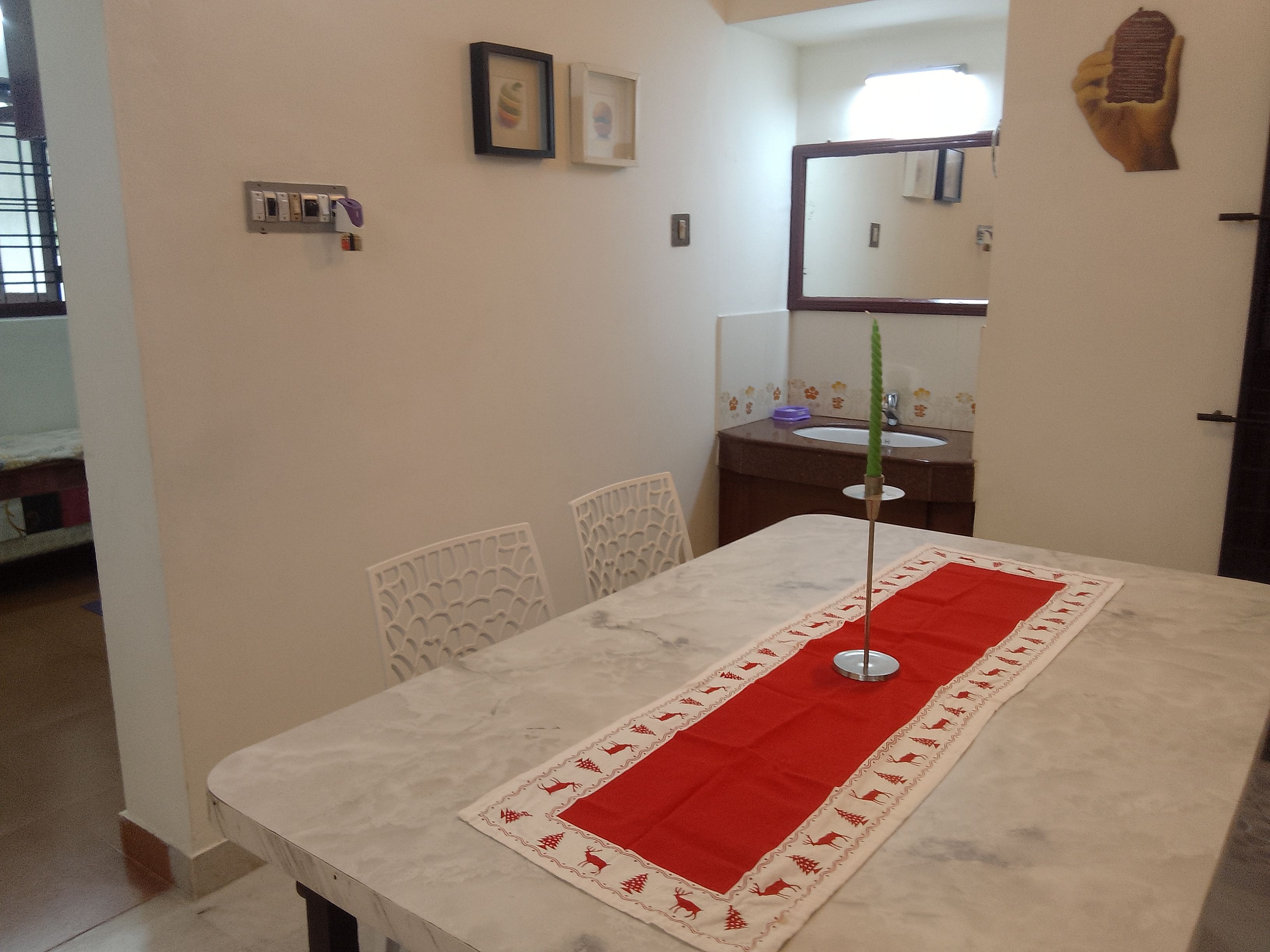 Un comedor con una mesa lista para cuatro personas, un espejo y un lavamanos al fondo.