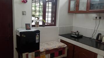 A compact kitchen with a refrigerator, a stove, and a window with a view of greenery outside.
