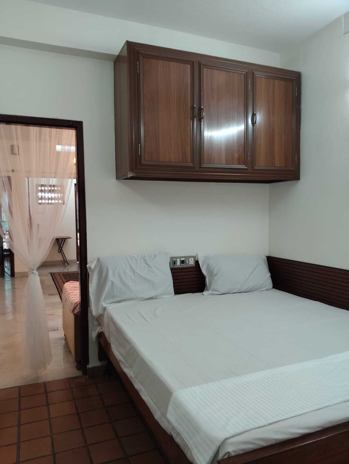Ein Schlafzimmer mit einem Bett, weißer Bettwäsche, einem Holzschrank und einem Fliesenboden.