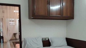 Un dormitorio con cama, ropa de cama blanca, un armario de madera y suelo de baldosas.