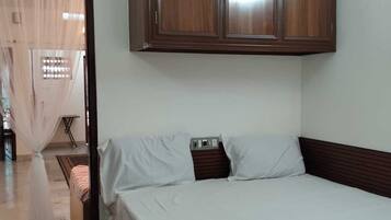 Ein Schlafzimmer mit einem Bett, weißer Bettwäsche, einem Holzschrank und einem Fliesenboden.
