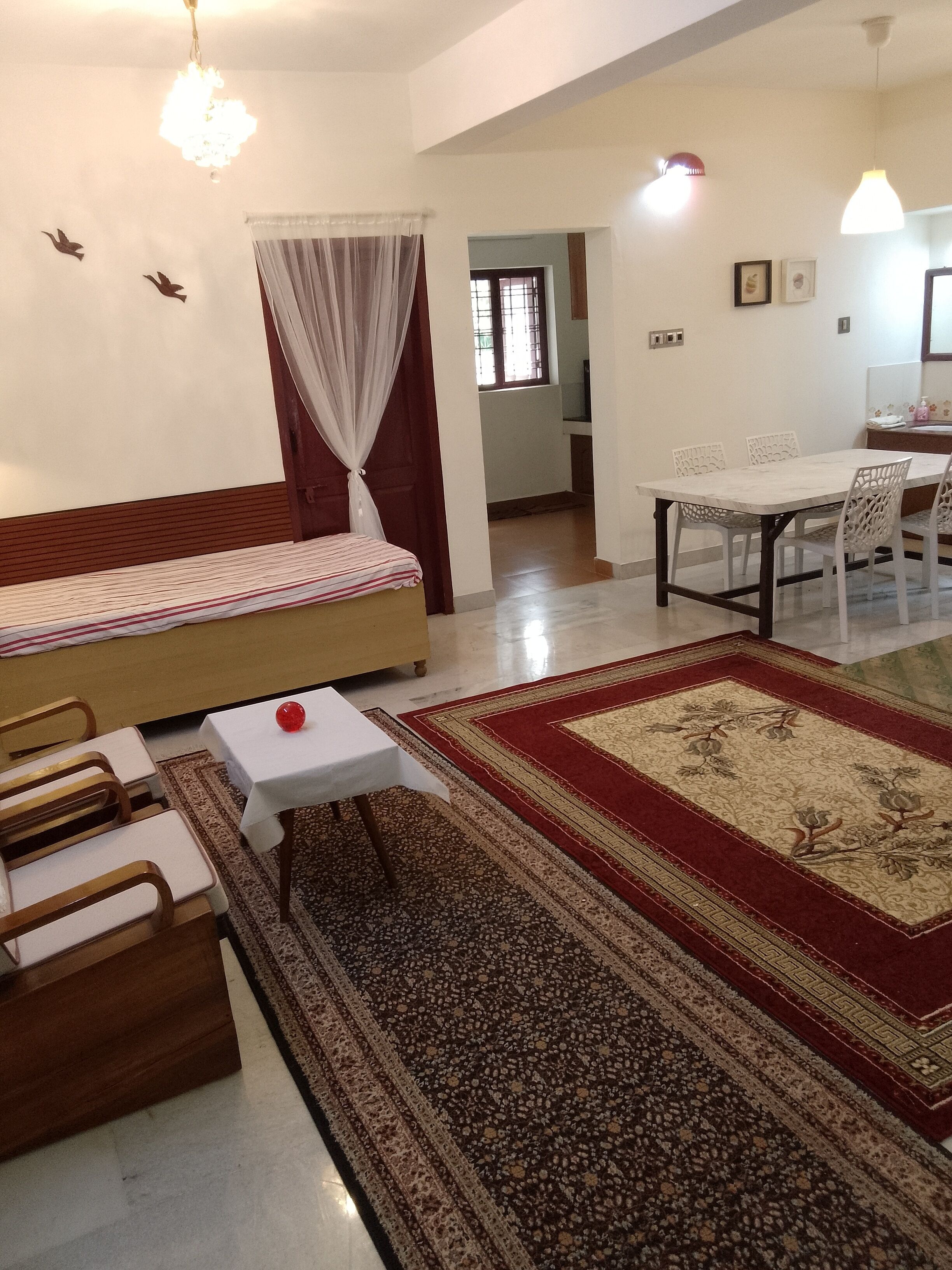 Ein Zimmer mit einem Bett, einem Esstisch mit Stühlen, einem kleinen weißen Tisch und einem gemusterten Teppich.
