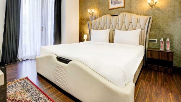 Ein Hotelzimmer mit einem großen Bett, einem Nachttisch, einer Lampe, einem gerahmten Bild an der Wand und einem Fenster mit Vorhängen.