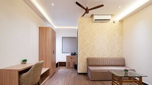 Ein modernes Wohnzimmer mit Sofa, Glastisch, Schreibtisch mit Stuhl, Deckenventilator und Klimaanlage.