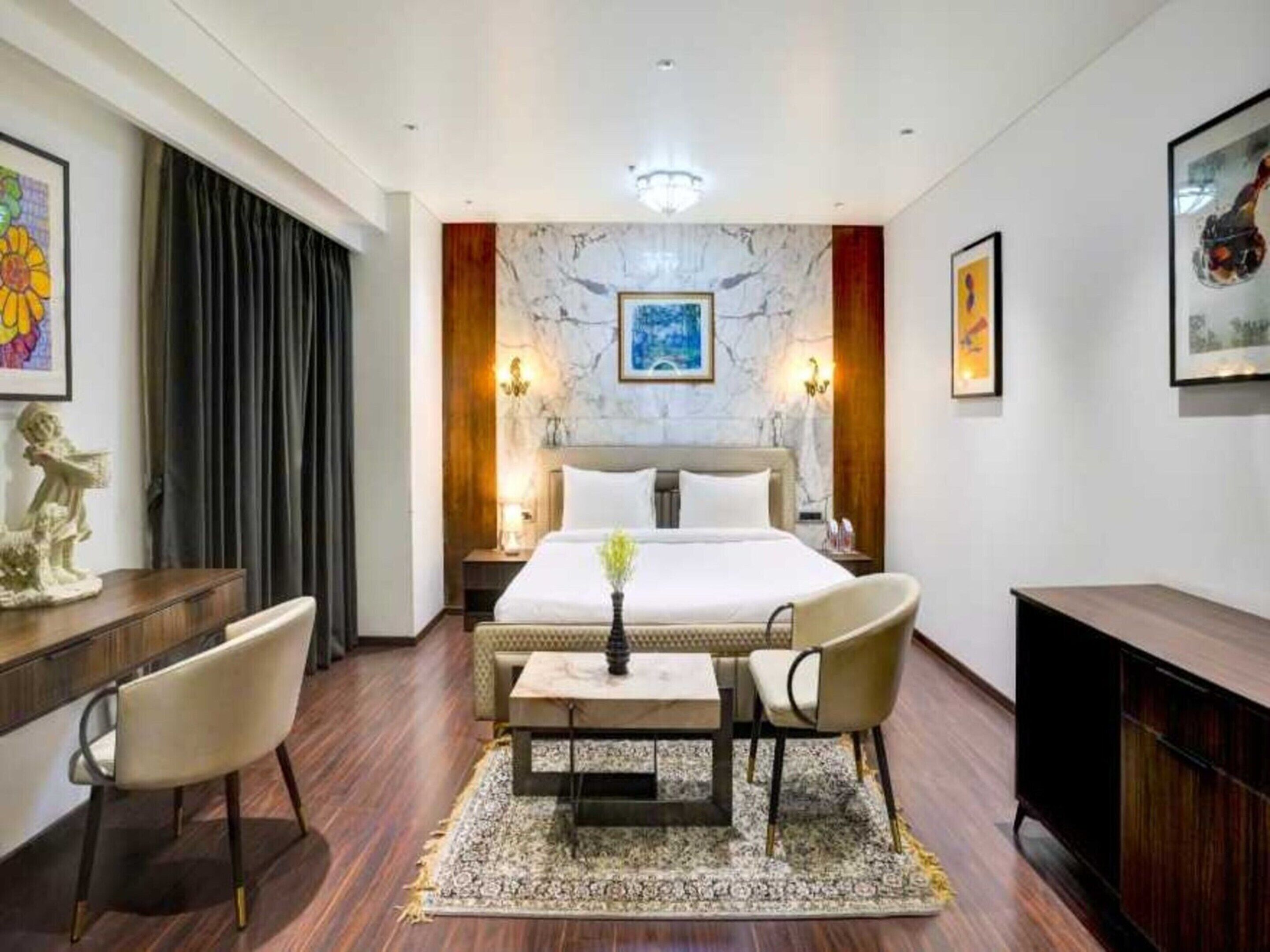 Una habitación de hotel con una cama grande, un escritorio con sillas, un televisor y obras de arte en las paredes.