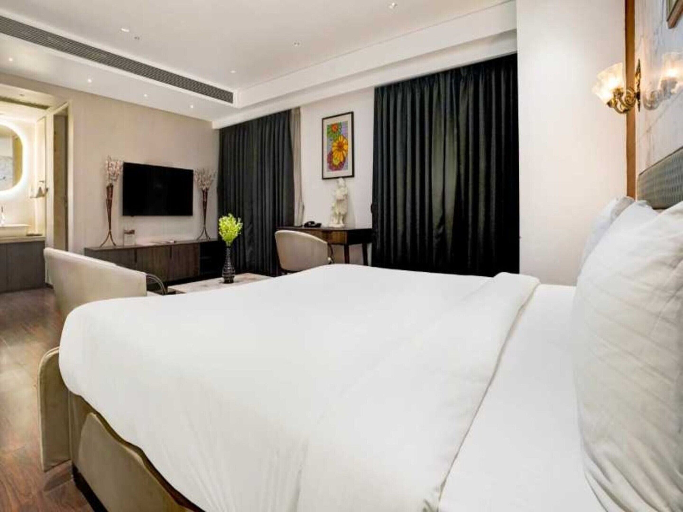 Camera d'albergo con un ampio letto, una scrivania, una sedia, un televisore e una finestra con tende.