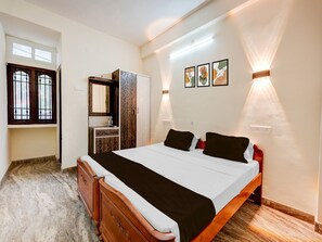 A bedroom with a bed, dresser, vanity, and artwork on the wall. - Premiumannakilly Tower Guest House (Chennai)