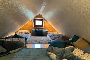 A cozy attic bedroom with a sloped ceiling, a small window, and a bed with multiple pillows and a plush shark toy. - Grünberg on the Jepsen holiday farm (Westerholz)