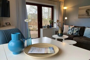 Ein modernes Wohnzimmer mit einer Couch, einem Couchtisch, einem Fernseher und einem Fenster mit Vorhängen.