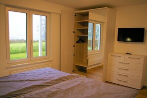 A bedroom with a bed, a wardrobe, a television, and a window with a view of greenery. - Holiday home with 2 bedrooms (Klein Wittensee)