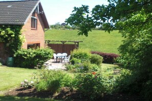 Ein Ziegelhaus mit Terrasse, umgeben von einem gepflegten Garten mit verschiedenen Pflanzen und einem Holzzaun.
