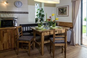 A wooden dining table with chairs, a clock, a plant, and a framed picture on the wall.