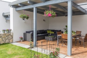 An outdoor patio area with a sofa, dining table, and chairs, surrounded by hanging planters and a stone wall.