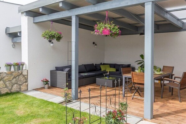 An outdoor patio area with a sofa, dining table, and chairs, surrounded by hanging planters and a stone wall.
