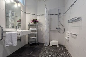 A modern bathroom with a shower, a sink with a towel rack, and a small stool.