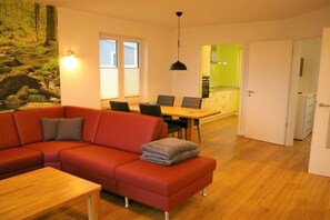 A modern living room with a red sofa, a wooden coffee table, and a dining area with a table and chairs. - Holiday home with 2 bedrooms (Klein Wittensee)