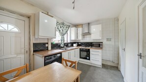 A compact kitchen with white cabinets, a wooden dining table, and a microwave. - 2 Bed House - Sleeps 4 - Parking - Wifi (Sheffield)