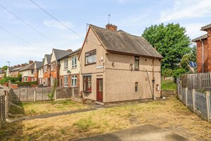 Ett bostadshus med en asfalterad uppfart, ett trästaket och en gräsyta.